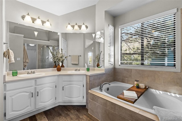 bathroom with double vanity, wood finished floors, a garden tub, a shower stall, and a sink