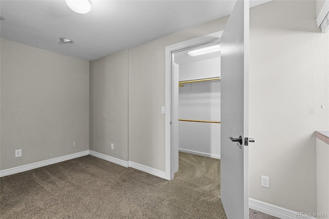 unfurnished bedroom with carpet floors, a closet, a spacious closet, and baseboards