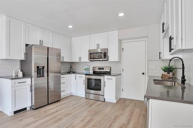 3575 S Ouray St, Aurora, CO 80013 - kitchen with appliances with stainless steel finishes, a sink, dark countertops, backsplash, and light wood-style flooring