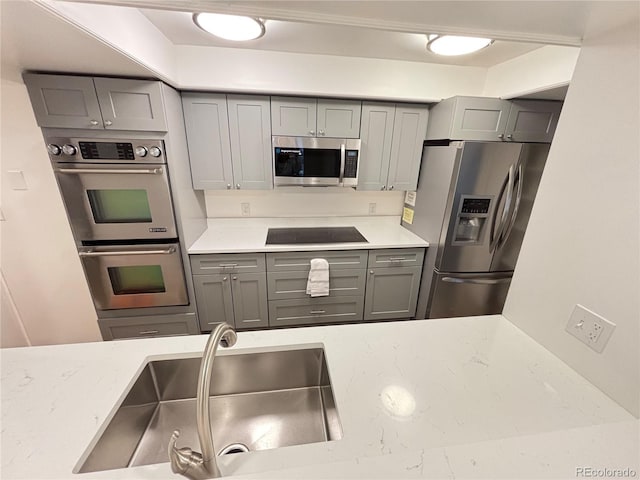 kitchen featuring appliances with stainless steel finishes, light stone counters, gray cabinetry, and sink