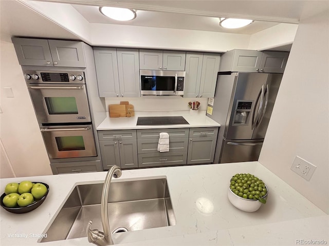 kitchen featuring stainless steel appliances, a sink, light stone counters, and gray cabinetry