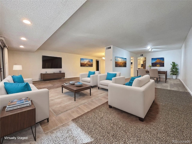 living area with a textured ceiling, recessed lighting, wood finished floors, visible vents, and baseboards