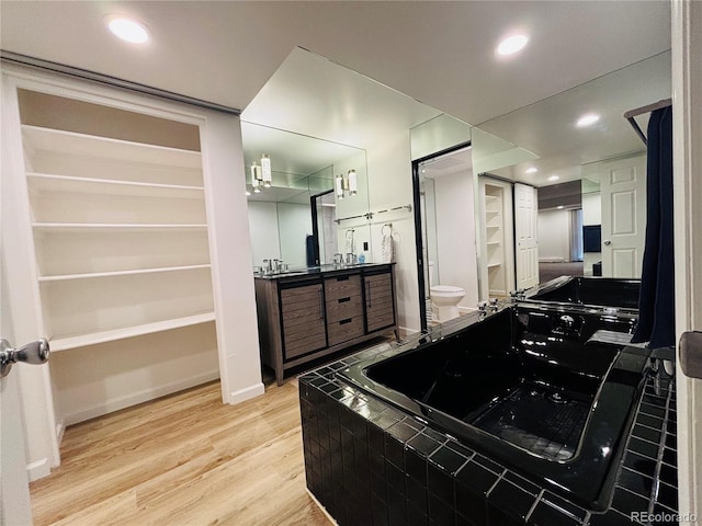 bathroom with tiled bath, recessed lighting, toilet, vanity, and wood finished floors