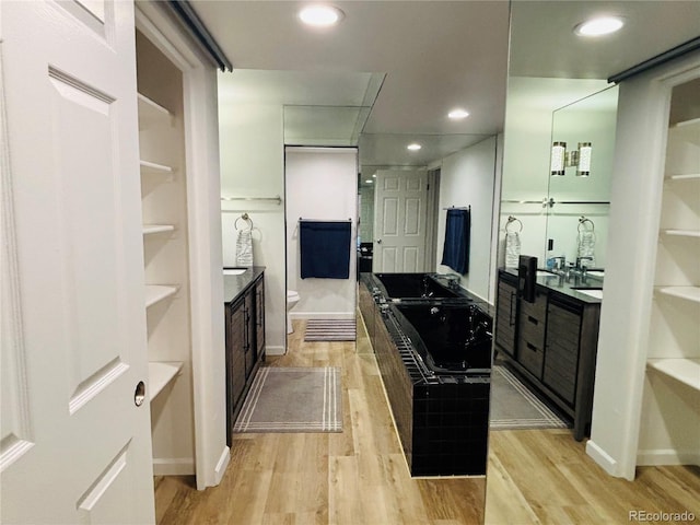 kitchen featuring light wood finished floors, dark countertops, recessed lighting, a sink, and baseboards