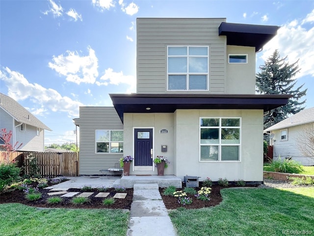 contemporary house with fence, a front lawn, and stucco siding