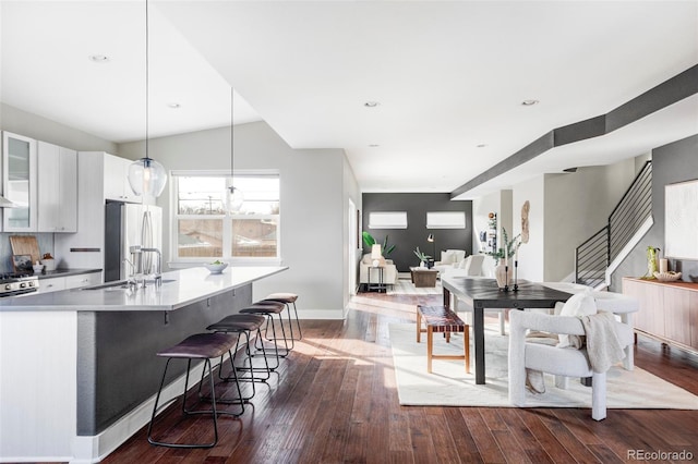 kitchen with decorative light fixtures, dark wood-type flooring, freestanding refrigerator, white cabinets, and an island with sink