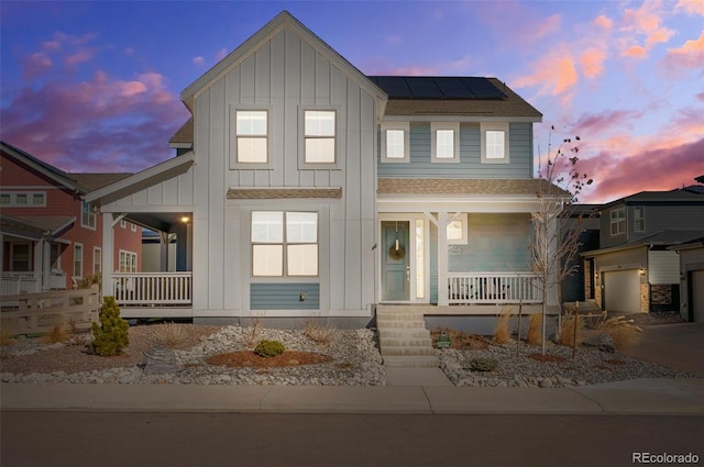 view of front of house with covered porch, a shingled roof, roof mounted solar panels, and board and batten siding