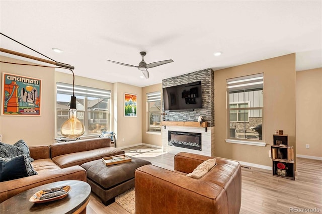 living room with light wood-style floors, a fireplace, baseboards, and ceiling fan