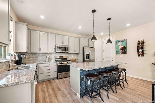 kitchen featuring stainless steel appliances, backsplash, a sink, a kitchen island, and a kitchen bar