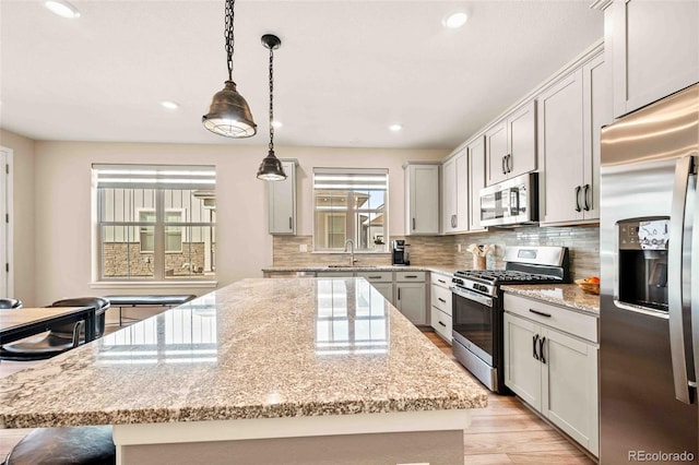 kitchen with light stone counters, stainless steel appliances, a center island, tasteful backsplash, and pendant lighting