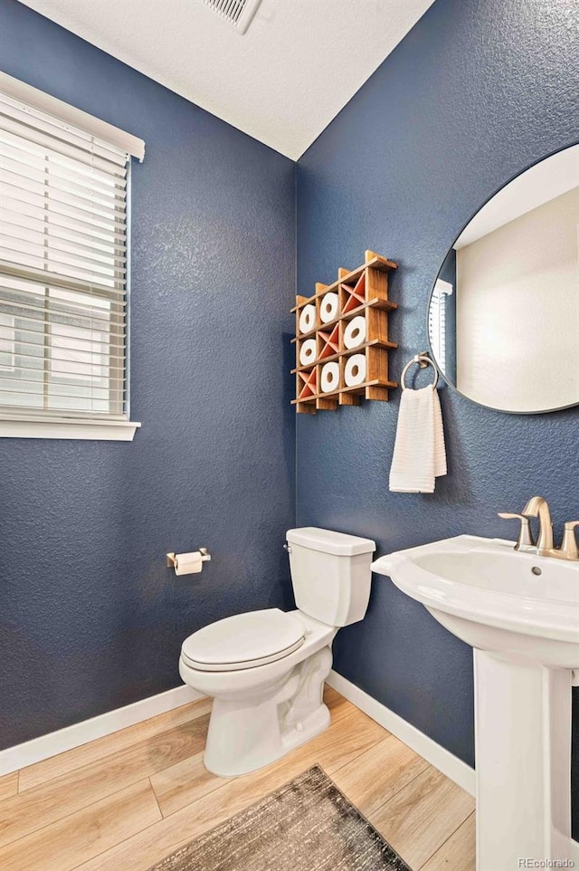 bathroom with baseboards, a textured wall, toilet, wood finished floors, and a wealth of natural light