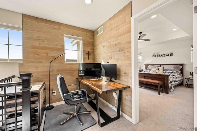 home office featuring wood walls, visible vents, baseboards, a ceiling fan, and carpet