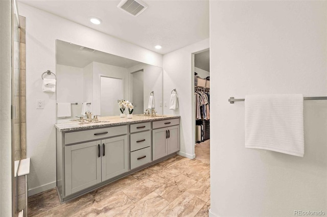 bathroom with a sink, visible vents, baseboards, double vanity, and a walk in closet