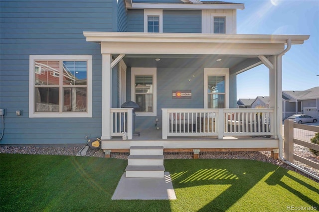 doorway to property with covered porch, a lawn, and fence