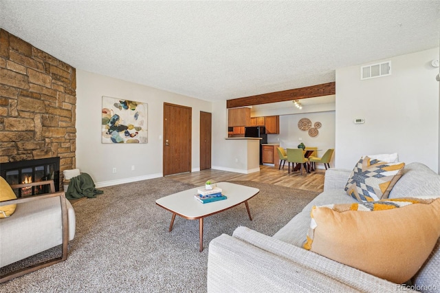 living room featuring visible vents, baseboards, a textured ceiling, and a stone fireplace