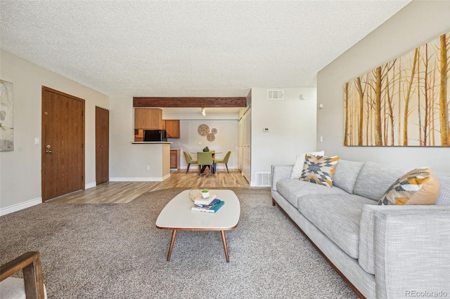living room with visible vents, baseboards, a textured ceiling, and light colored carpet