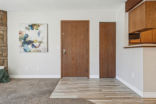 interior space featuring baseboards, a textured ceiling, and light wood finished floors