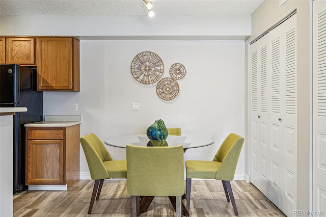 dining room with a textured ceiling, light wood-type flooring, and baseboards