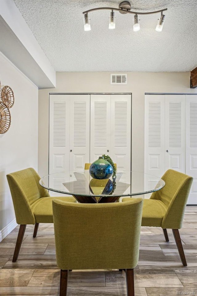 dining room featuring baseboards, wood finished floors, visible vents, and a textured ceiling