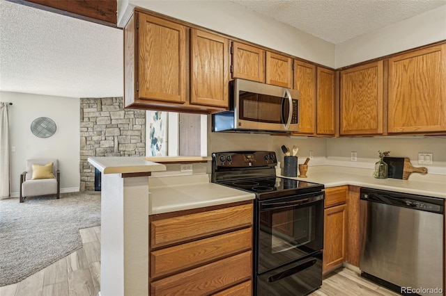 kitchen featuring brown cabinets, a textured ceiling, stainless steel appliances, light wood-style floors, and light countertops