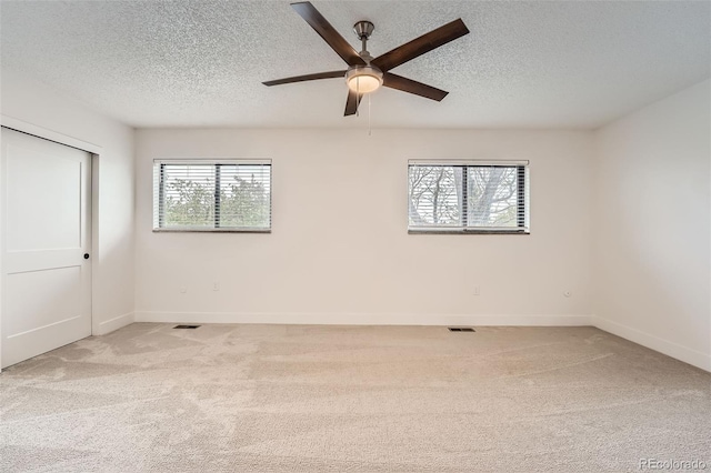 spare room with a textured ceiling, light colored carpet, ceiling fan, and baseboards