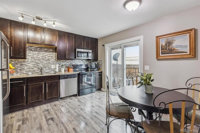 kitchen featuring appliances with stainless steel finishes, sink, light stone countertops, dark brown cabinetry, and tasteful backsplash