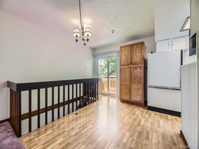 interior space with a textured ceiling, a chandelier, light wood finished floors, baseboards, and an upstairs landing