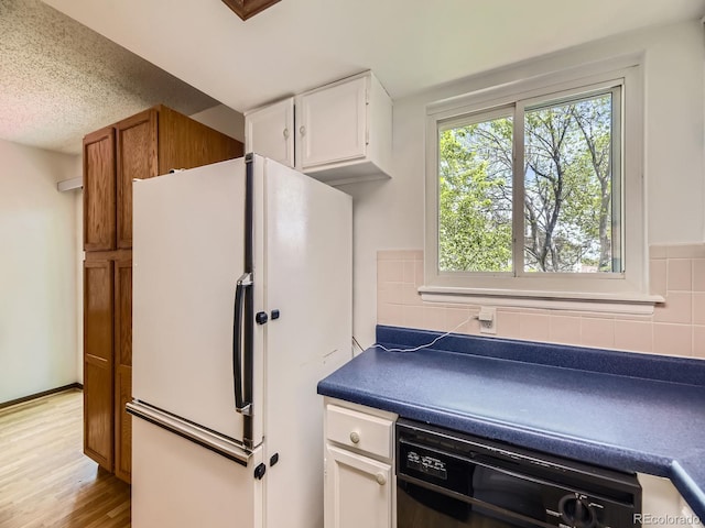 kitchen with freestanding refrigerator, black dishwasher, white cabinetry, dark countertops, and light wood-style flooring