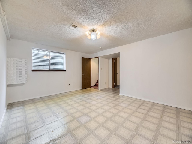 empty room featuring a textured ceiling, baseboards, and light flooring