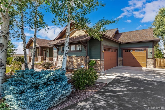 craftsman inspired home featuring roof with shingles, driveway, stone siding, fence, and a garage
