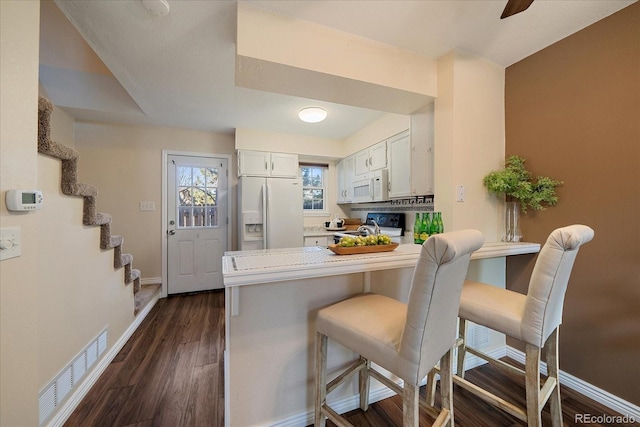 kitchen with visible vents, dark wood-type flooring, white cabinets, white appliances, and a peninsula