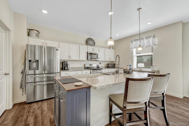 kitchen featuring an island with sink, white cabinets, stainless steel appliances, and decorative light fixtures