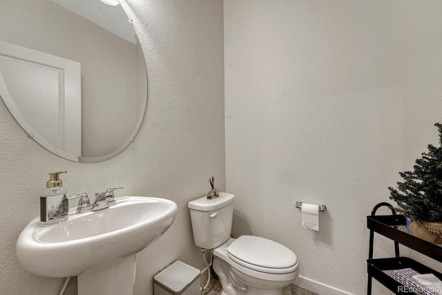 half bathroom with baseboards, toilet, a textured wall, and a sink