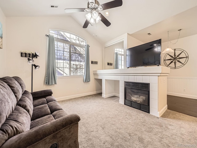 living room with carpet, visible vents, a fireplace, vaulted ceiling, and wainscoting