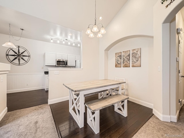 dining space with dark wood-style floors, a notable chandelier, wainscoting, and arched walkways