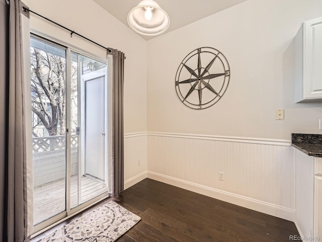 unfurnished dining area featuring a wainscoted wall and dark wood-type flooring