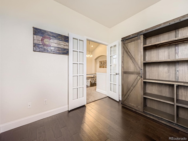 spare room featuring dark wood finished floors, a barn door, arched walkways, french doors, and baseboards