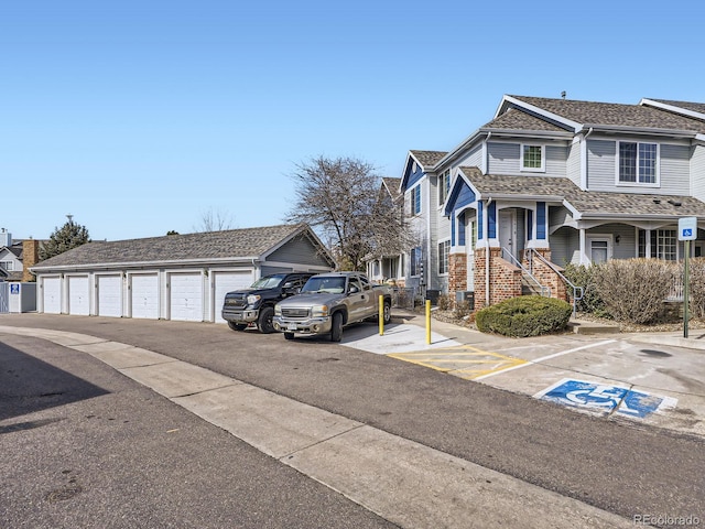 view of front of property with an outbuilding, community garages, a residential view, a shingled roof, and brick siding