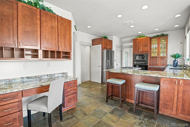 kitchen with built in desk, light stone counters, a breakfast bar area, black appliances, and sink