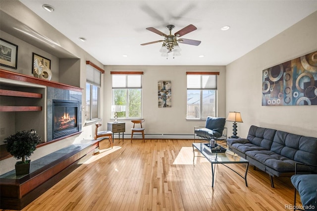 living room with baseboard heating, light hardwood / wood-style flooring, and ceiling fan