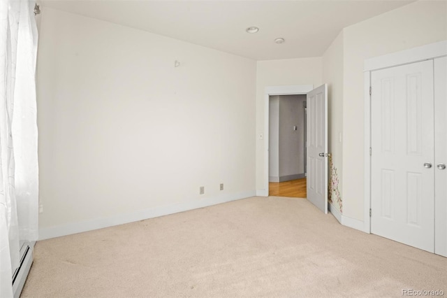 unfurnished bedroom with a closet, light carpet, and a baseboard heating unit