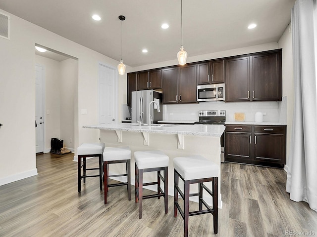 9844 Truckee St, Commerce City, CO 80022 - kitchen with dark brown cabinets, stainless steel appliances, light wood-style flooring, and a breakfast bar
