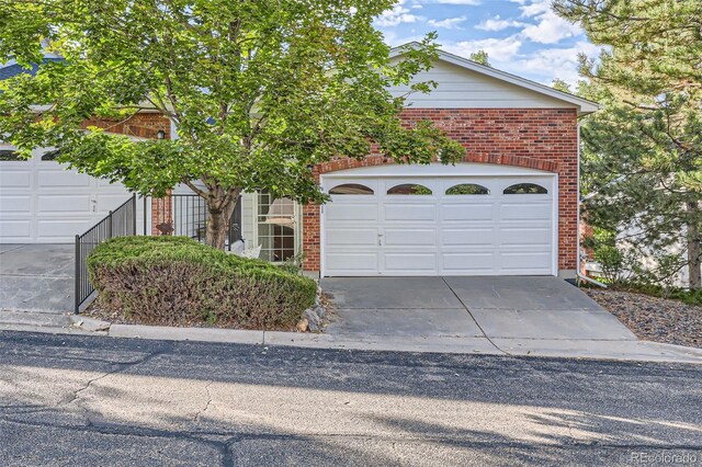 view of property hidden behind natural elements featuring brick siding, a garage, and driveway