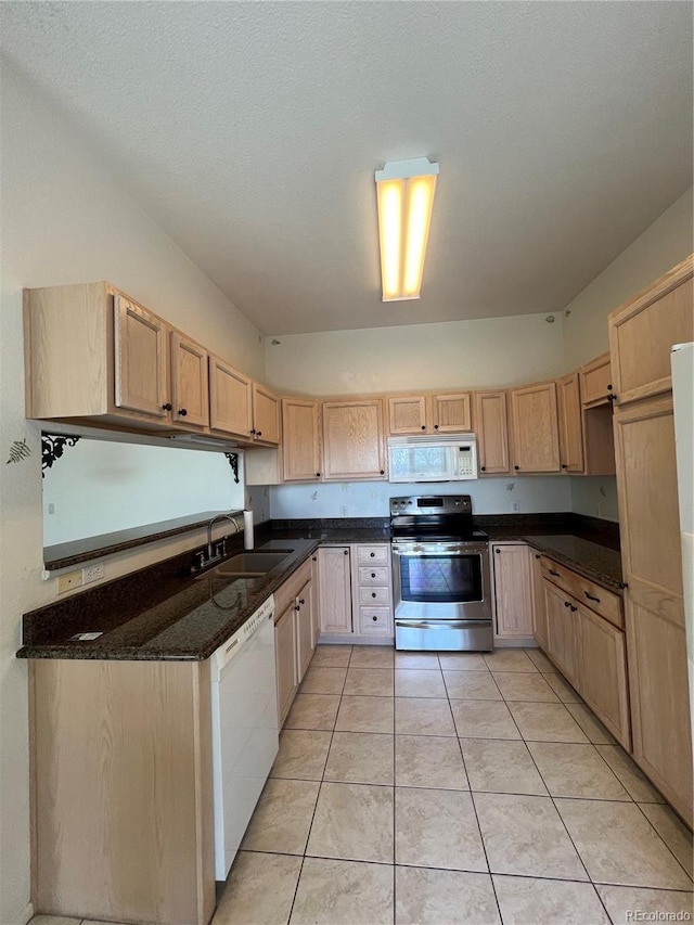 kitchen with white appliances, light tile patterned floors, dark stone counters, a sink, and light brown cabinetry
