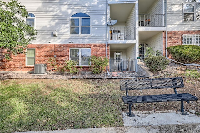 back of property featuring brick siding, central air condition unit, and a lawn