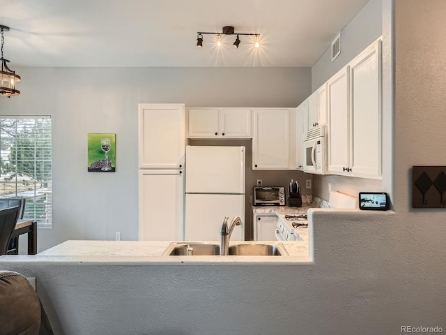 kitchen with visible vents, a sink, white appliances, white cabinets, and hanging light fixtures