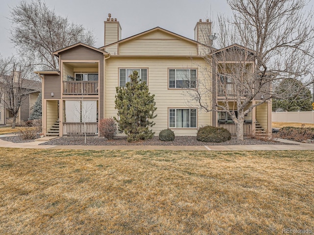 view of front of property with stairs, a front lawn, a balcony, and a chimney