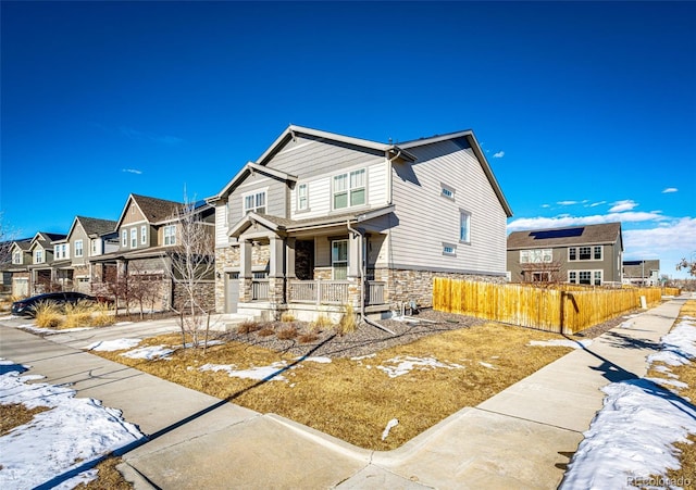 view of front of house featuring stone siding, a porch, fence, and a residential view