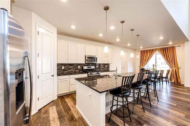 kitchen with stainless steel appliances, dark wood-type flooring, a breakfast bar, backsplash, and an island with sink