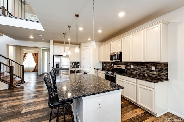 kitchen featuring dark wood-style floors, backsplash, appliances with stainless steel finishes, a sink, and an island with sink